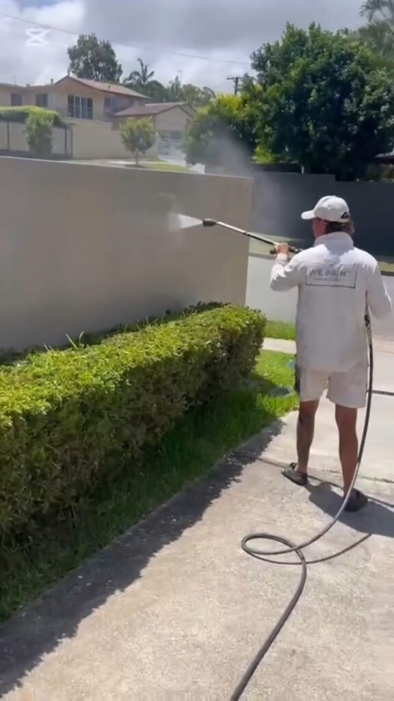 We Paint Gold Coast painter pressure washing a rendered exterior wall before repainting