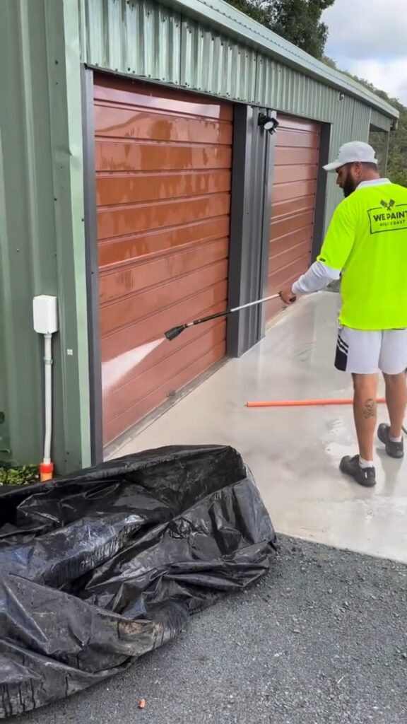 We Paint Gold Coast painter pressure washing rusty roller doors on a shed before repainting