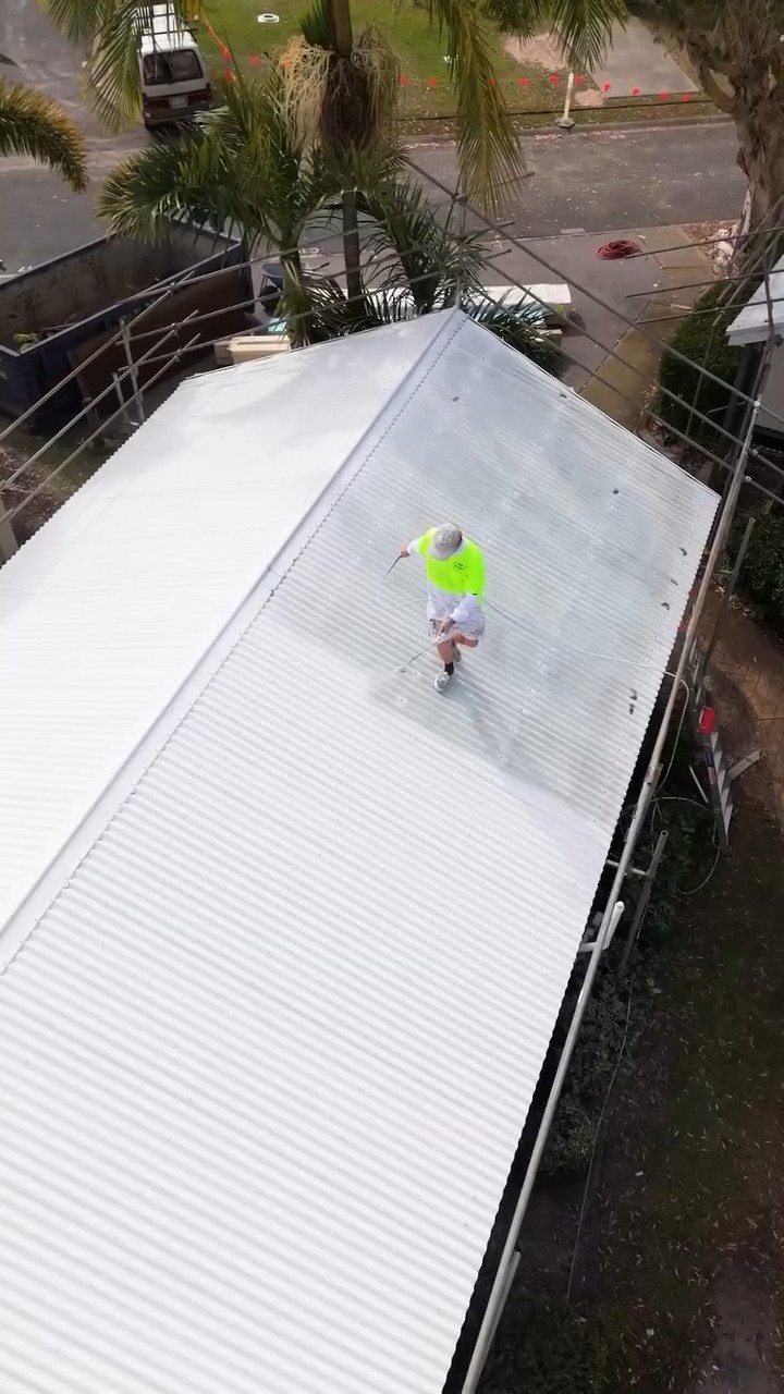 We Paint Gold Coast painter spray coating a cabin roof at Tallebudgera Creek, aerial view