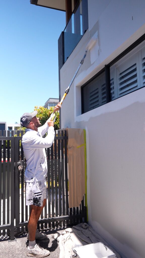 We Paint Gold Coast painter rolling the upper exterior wall of a Southport home